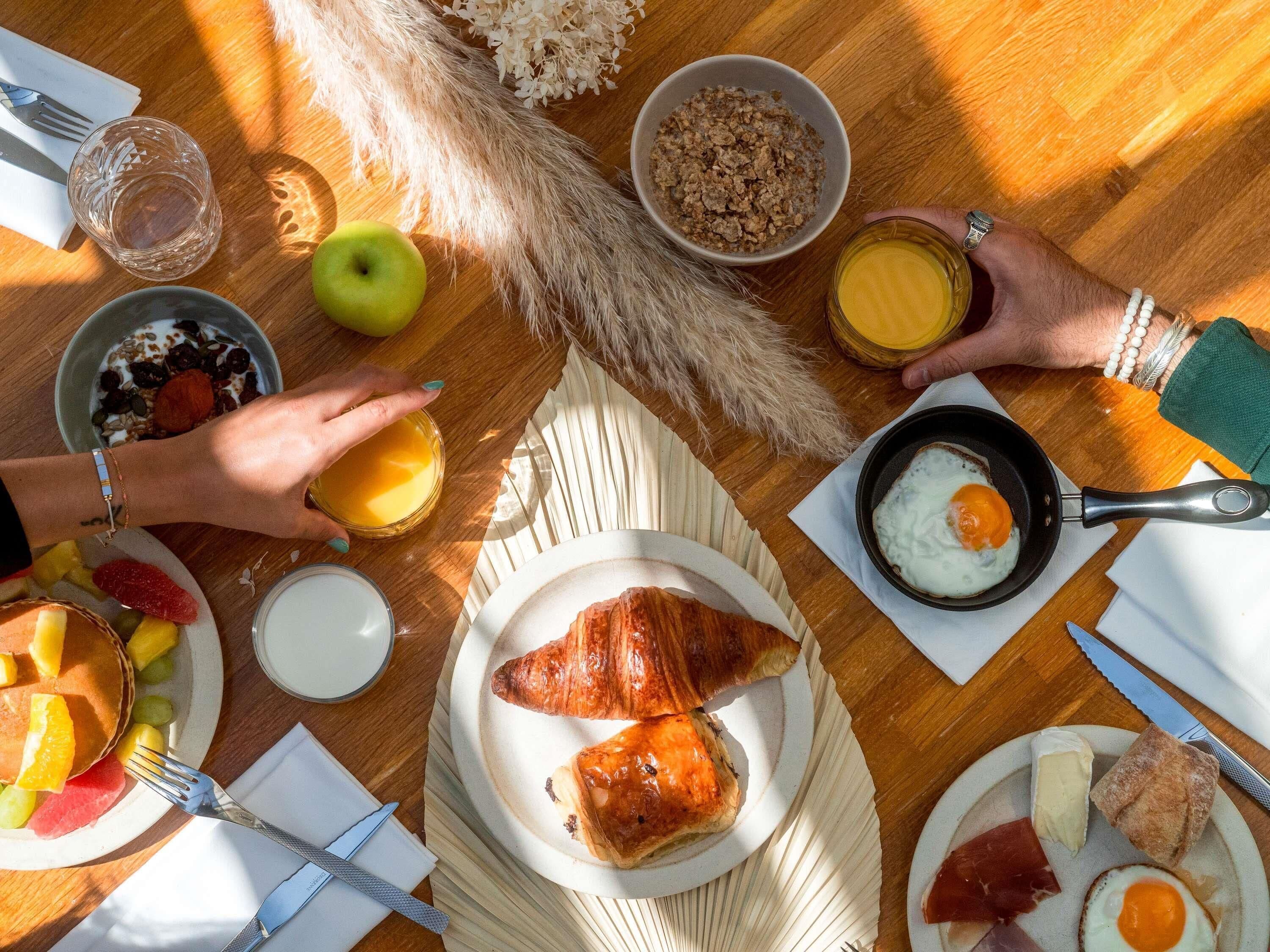 Un desayuno con platos de comida, un tazón de cereal, un vaso de jugo y una sartén con un huevo.