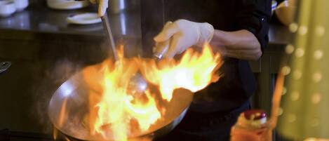 Un cocinero preparando comida en una sartén wok sobre una estufa, rodeado de utensilios y productos frescos.