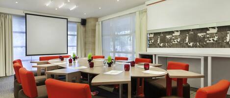 A conference room with a large table, red chairs, a projector screen, and a large window.