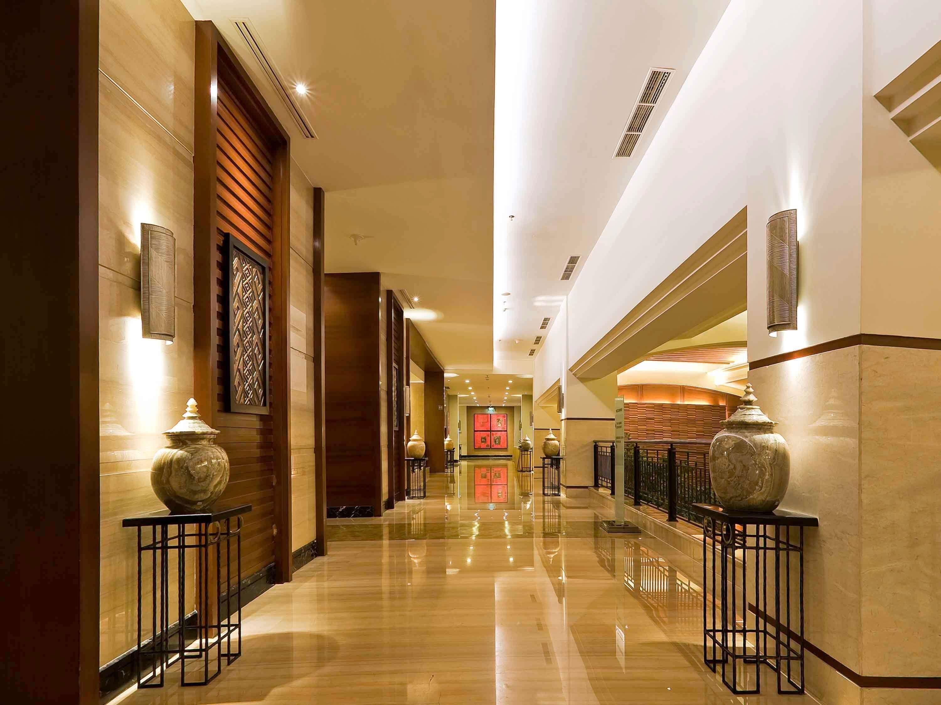 A hotel corridor with polished floors, wooden paneling, and decorative vases on stands.