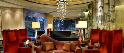 A luxurious lobby with a red sofa, two armchairs, a round coffee table, and a grand piano.