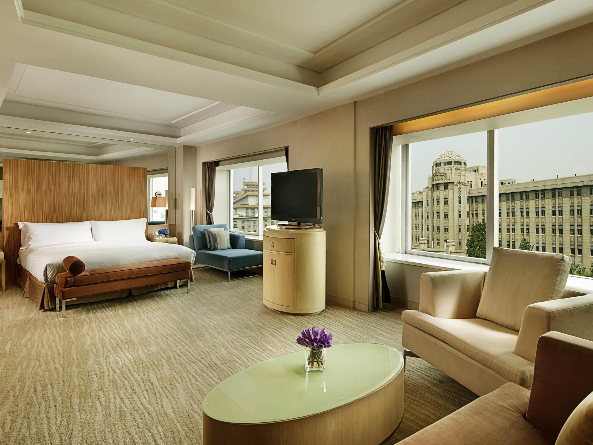 A hotel room with a bed, a TV, a sofa, a coffee table, and a view of a cityscape.