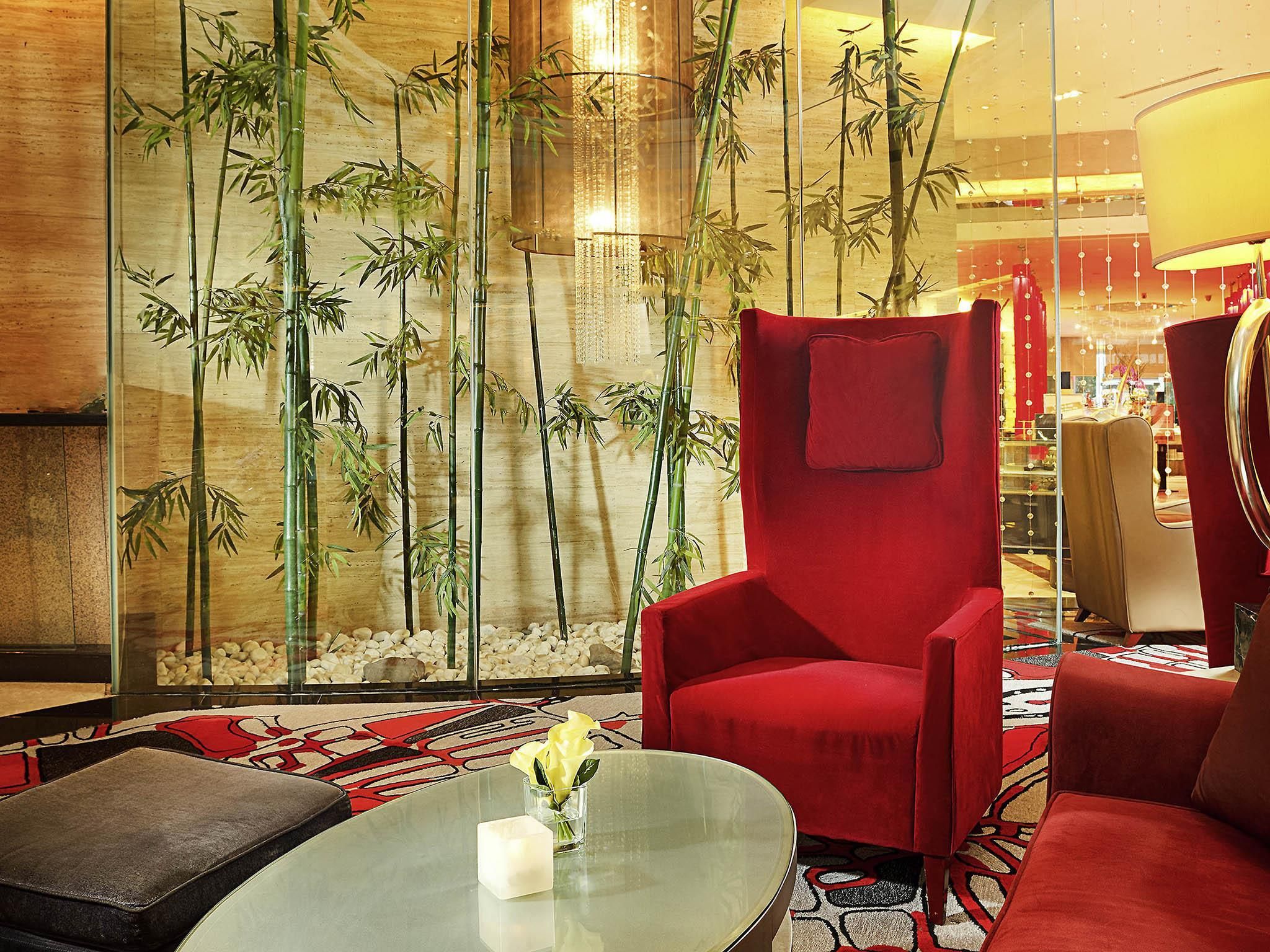 Un interior moderno con un sillón rojo, una mesita de centro de vidrio y una pared decorada con plantas de bambú.
