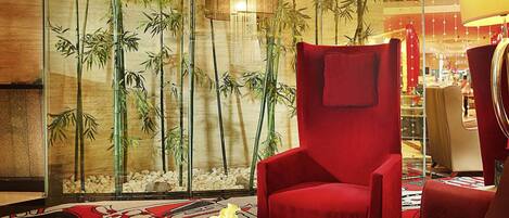 Un interior moderno con un sillón rojo, una mesita de centro de vidrio y una pared decorada con plantas de bambú.