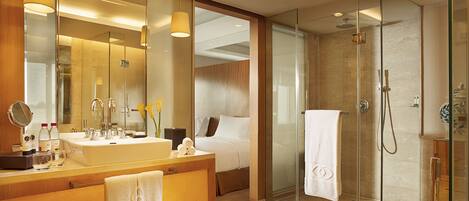 A modern hotel bathroom with a large sink, mirror, and glass shower enclosure.
