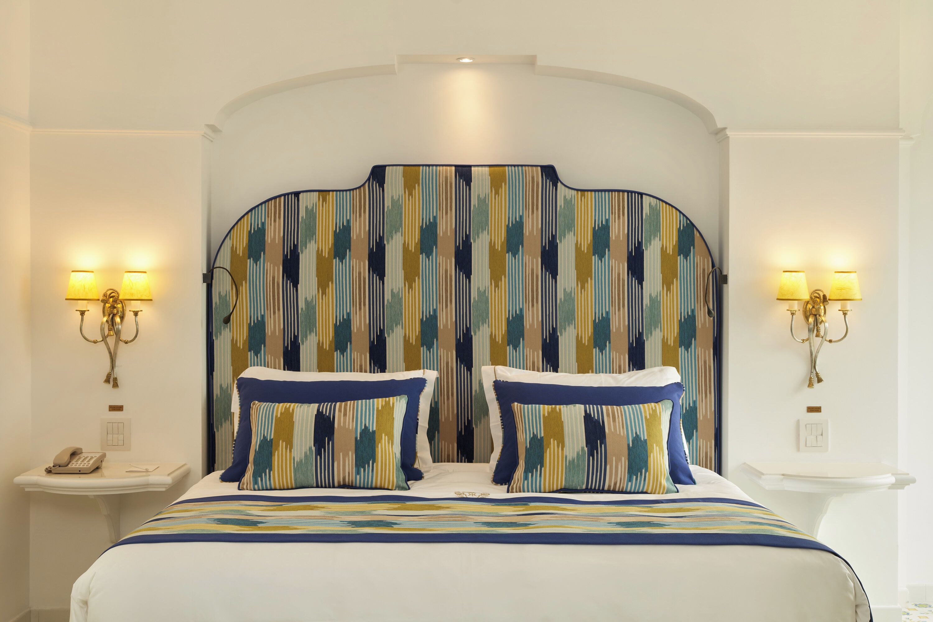 A hotel room with a large bed, two bedside lamps, a telephone, and a wall-mounted light fixture.