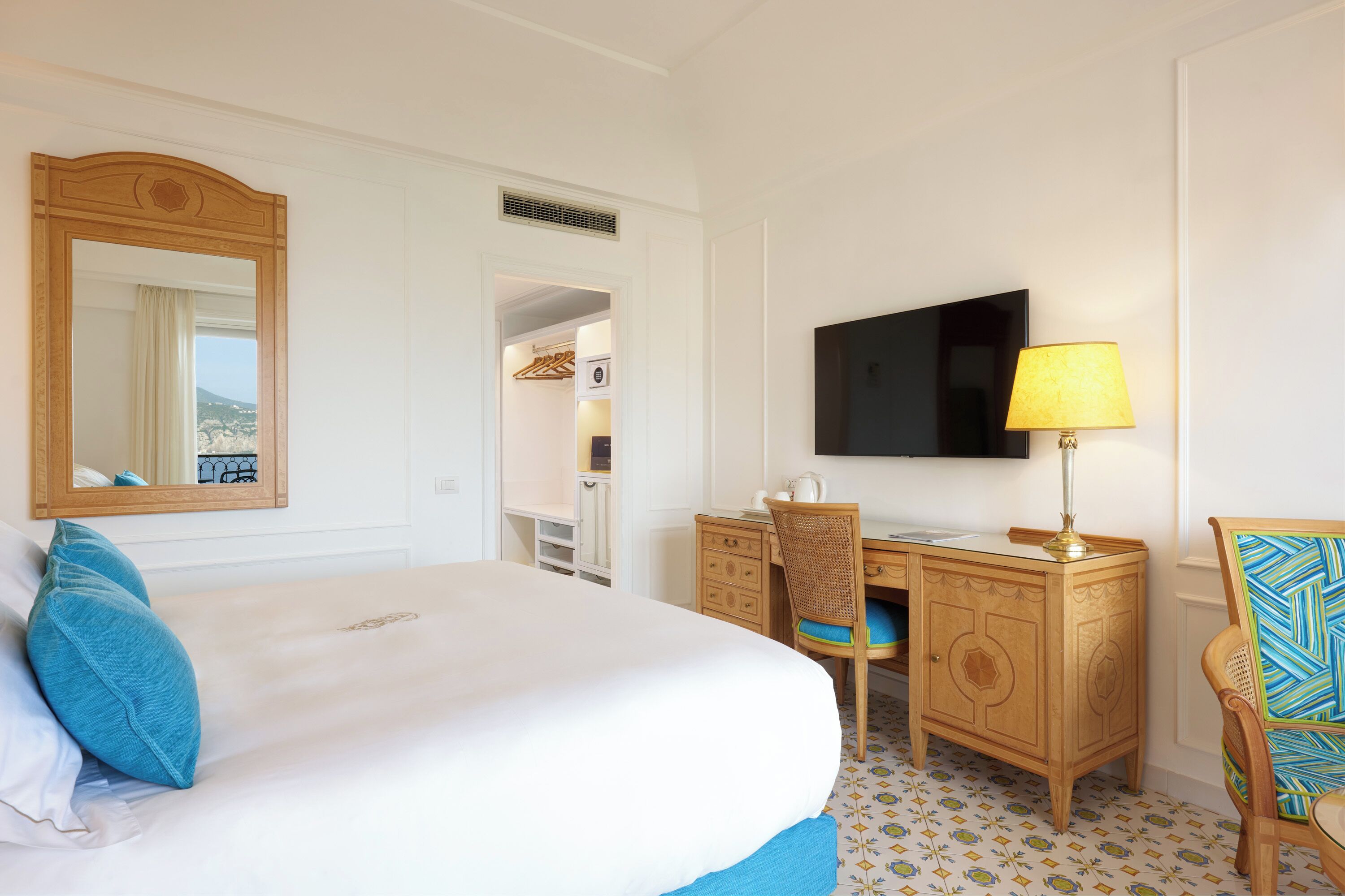 A hotel room with a large bed, a desk, a chair, a television, and a wardrobe.
