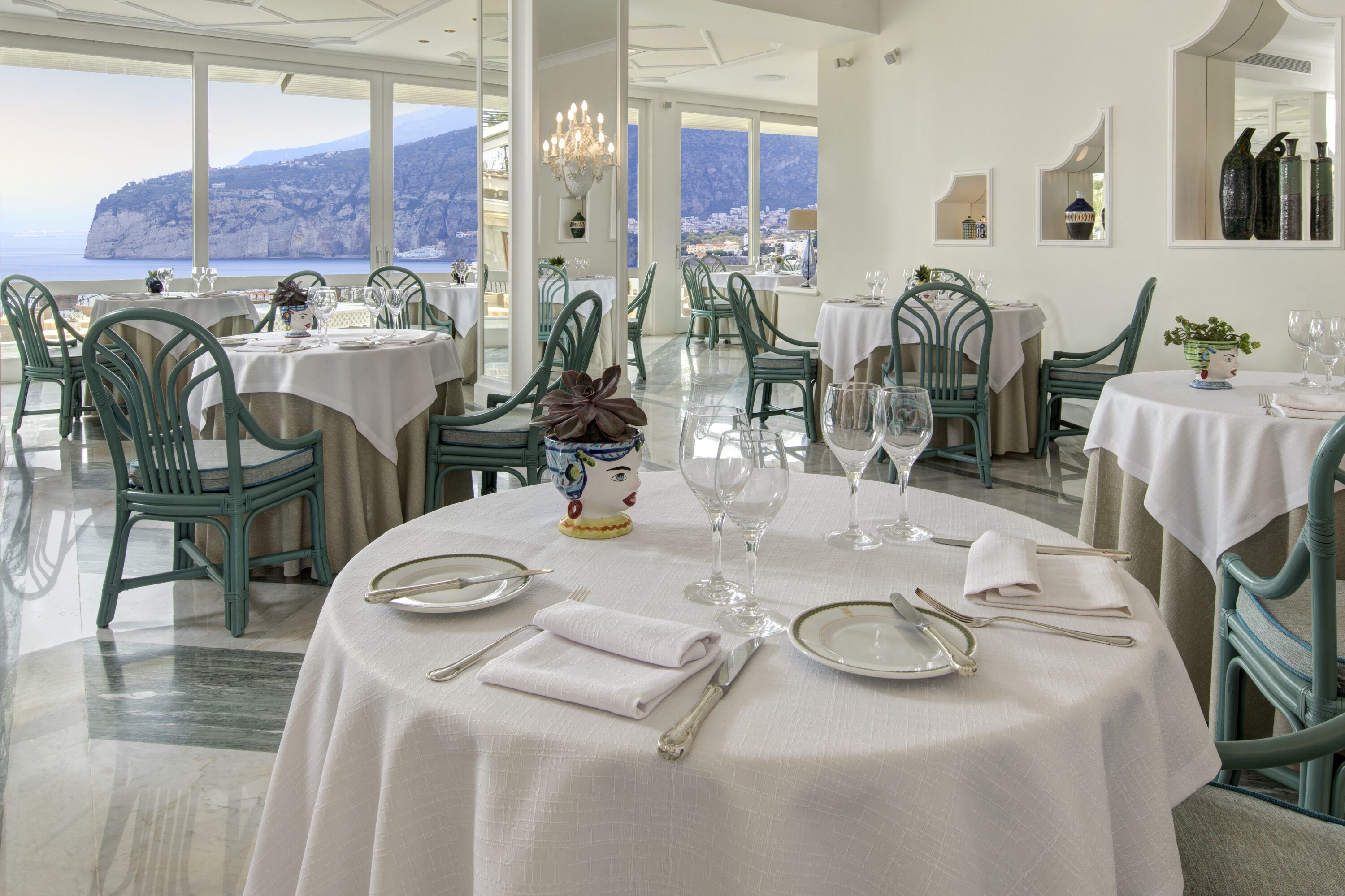 A restaurant with round tables, green chairs, and white tablecloths.