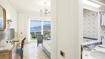 A hotel room with a balcony, a dining area, and a bathroom with a view of the sea.