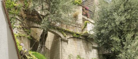 A garden with a stone bridge, lush greenery, and a building with a balcony.