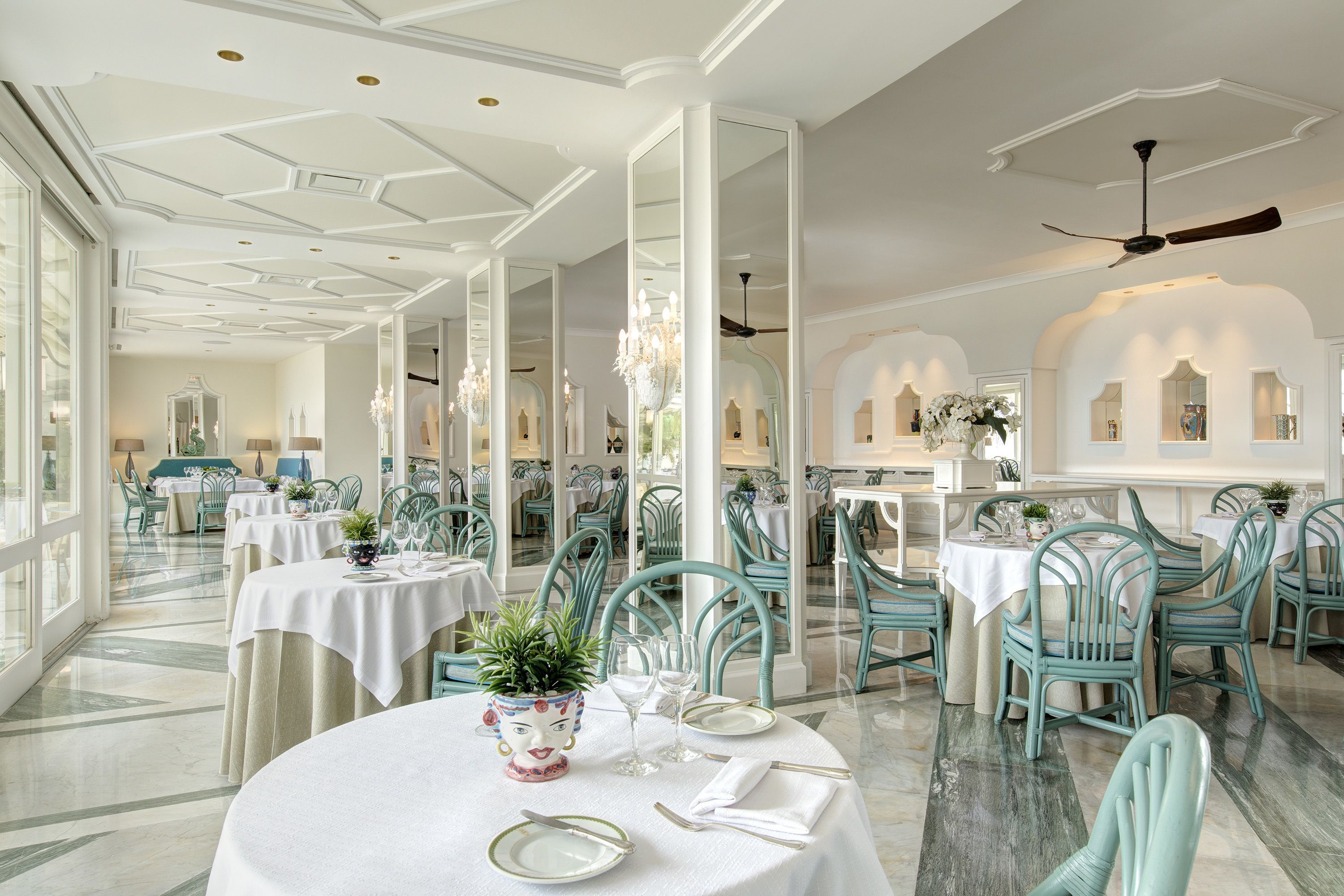 A spacious dining area with round tables, teal chairs, and a chandelier.