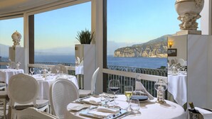 A dining area with tables set for a meal, overlooking a scenic coastal view. - Grand Hotel Capodimonte (Sorrento)