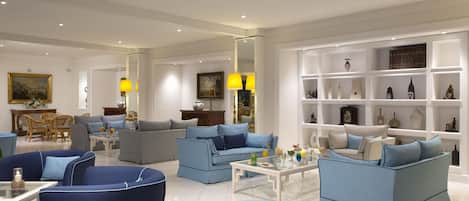 Un salón amplio con sofás azules, una mesa de centro blanca y una estantería llena de objetos decorativos.