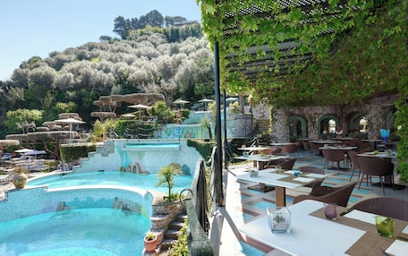 A poolside area with a pool, outdoor seating, and a view of a hillside.