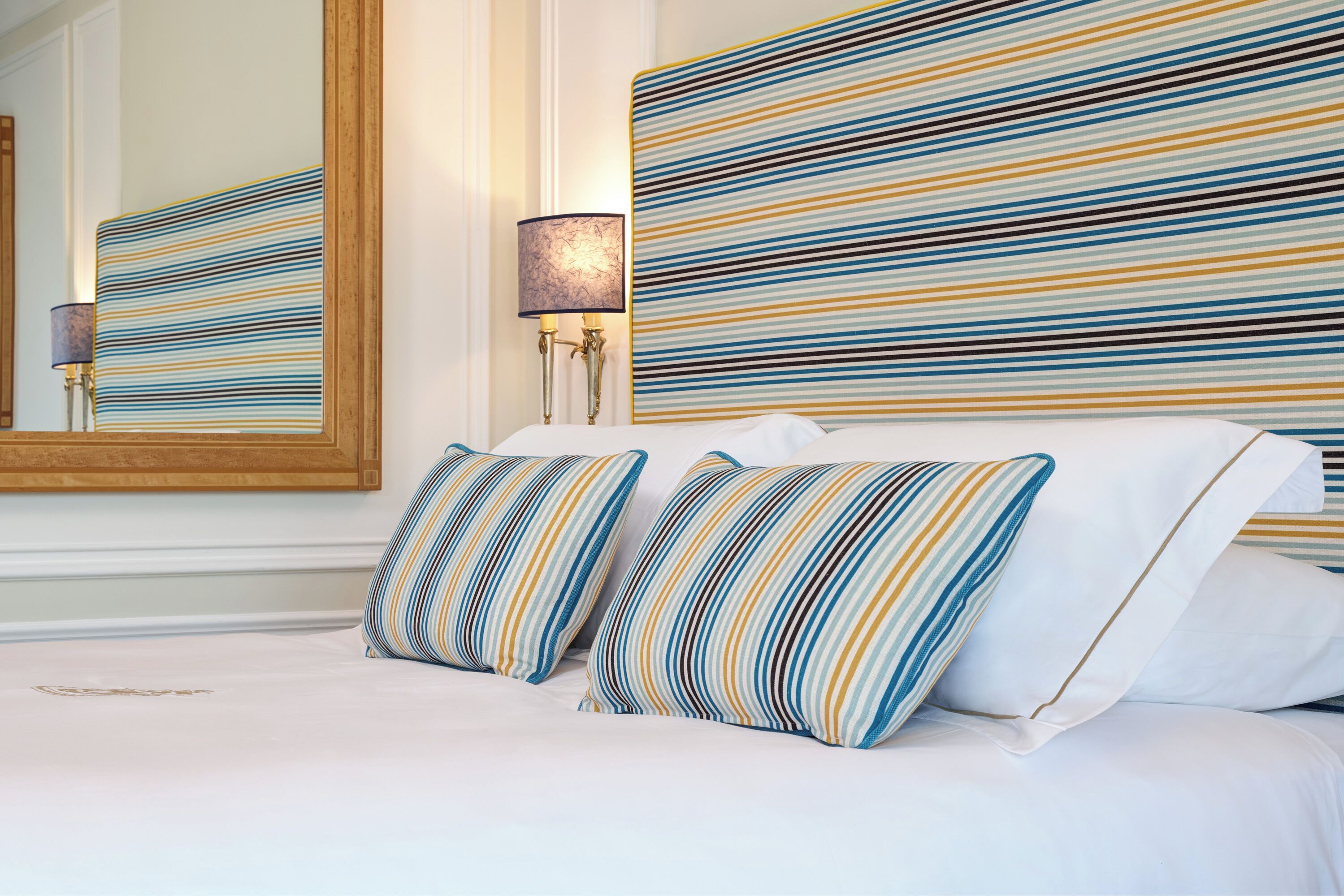 A neatly made bed with striped pillows and a large mirror on the wall.