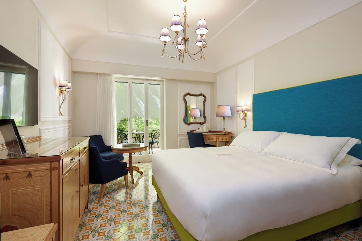 A hotel room with a large bed, a desk, a chair, a table, and a chandelier.