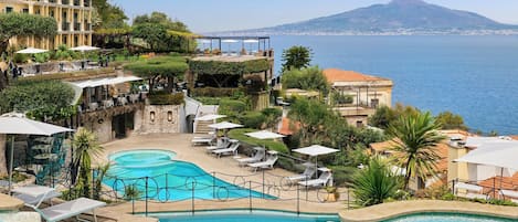 Un resort con una piscina grande, mobiliario exterior y vistas al mar y a una montaña.