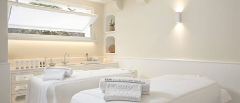 A hotel room with two beds, a vanity with toiletries, a window with a view, and a wall-mounted light.