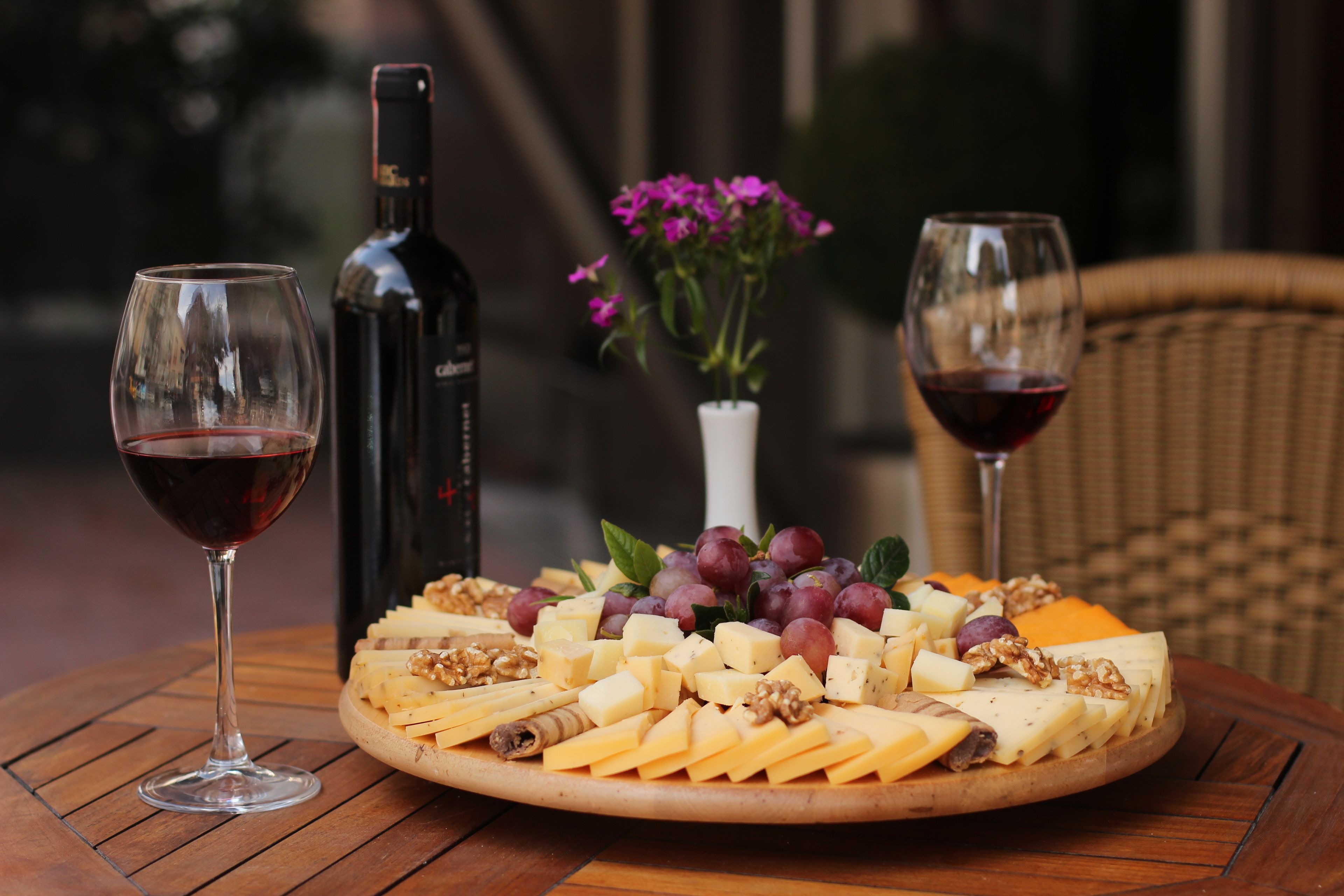 Un tagliere con formaggi, uva e noci su un tavolo di legno, accompagnato da due bicchieri da vino e una bottiglia.