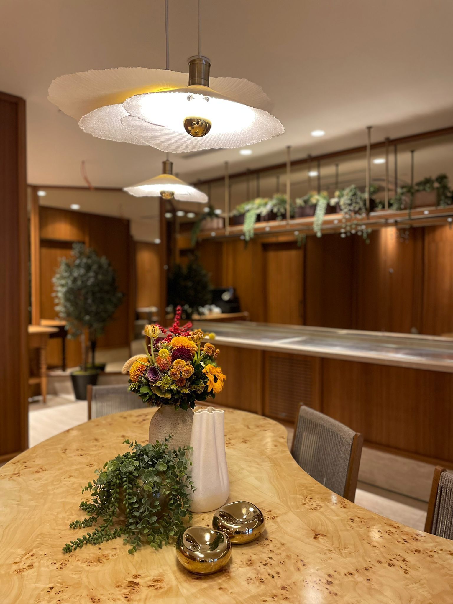 A dining area with a round wooden table, a vase of flowers, and two metallic bowls.