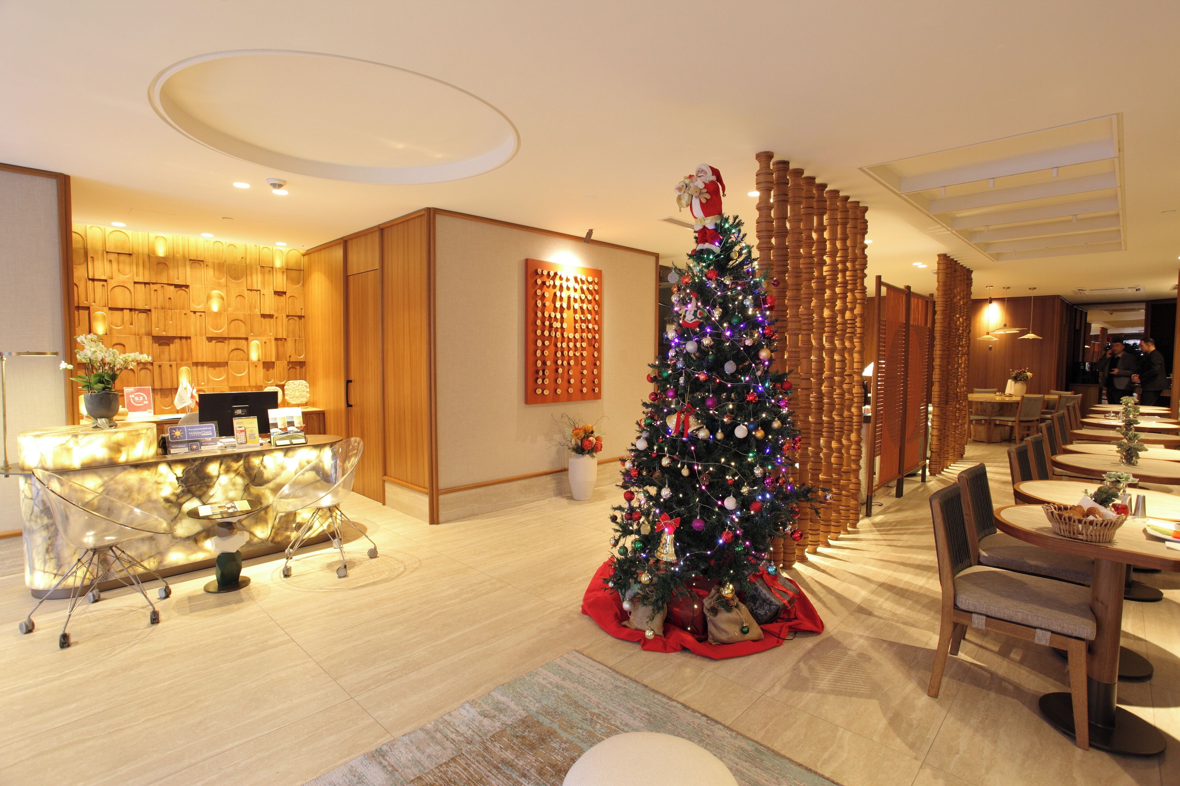 A hotel lobby with a reception desk, a Christmas tree, and a seating area with tables and chairs.