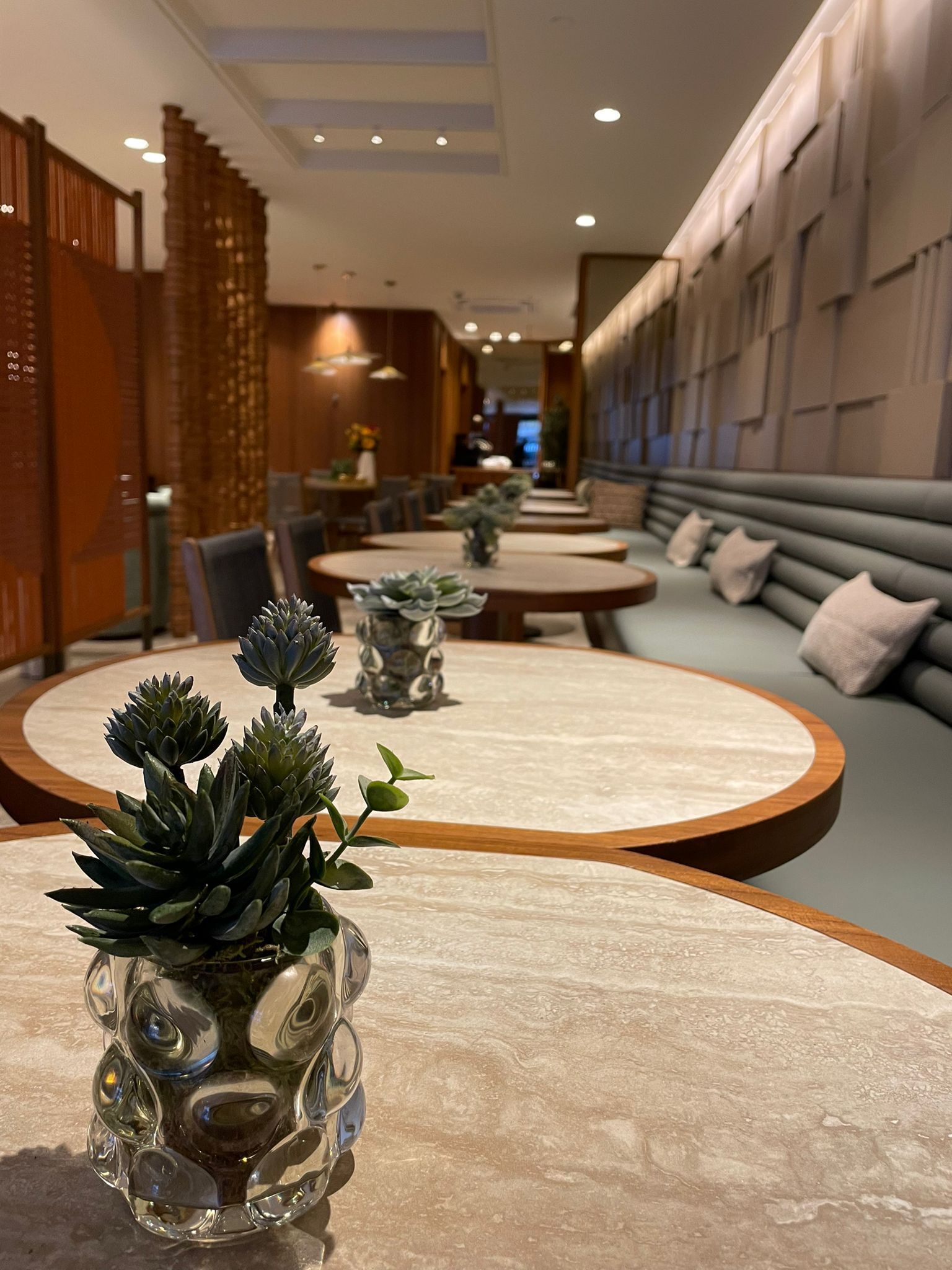 A modern hotel lobby with round tables, a seating area, and decorative plants.