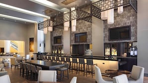 A modern bar area with a long counter, multiple seating options, and a large screen. - Marriott Hartford Downtown (Hartford)