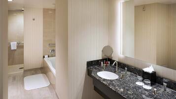 Un baño moderno con encimera de granito, dos lavamanos, un espejo grande y una ducha a ras de suelo.