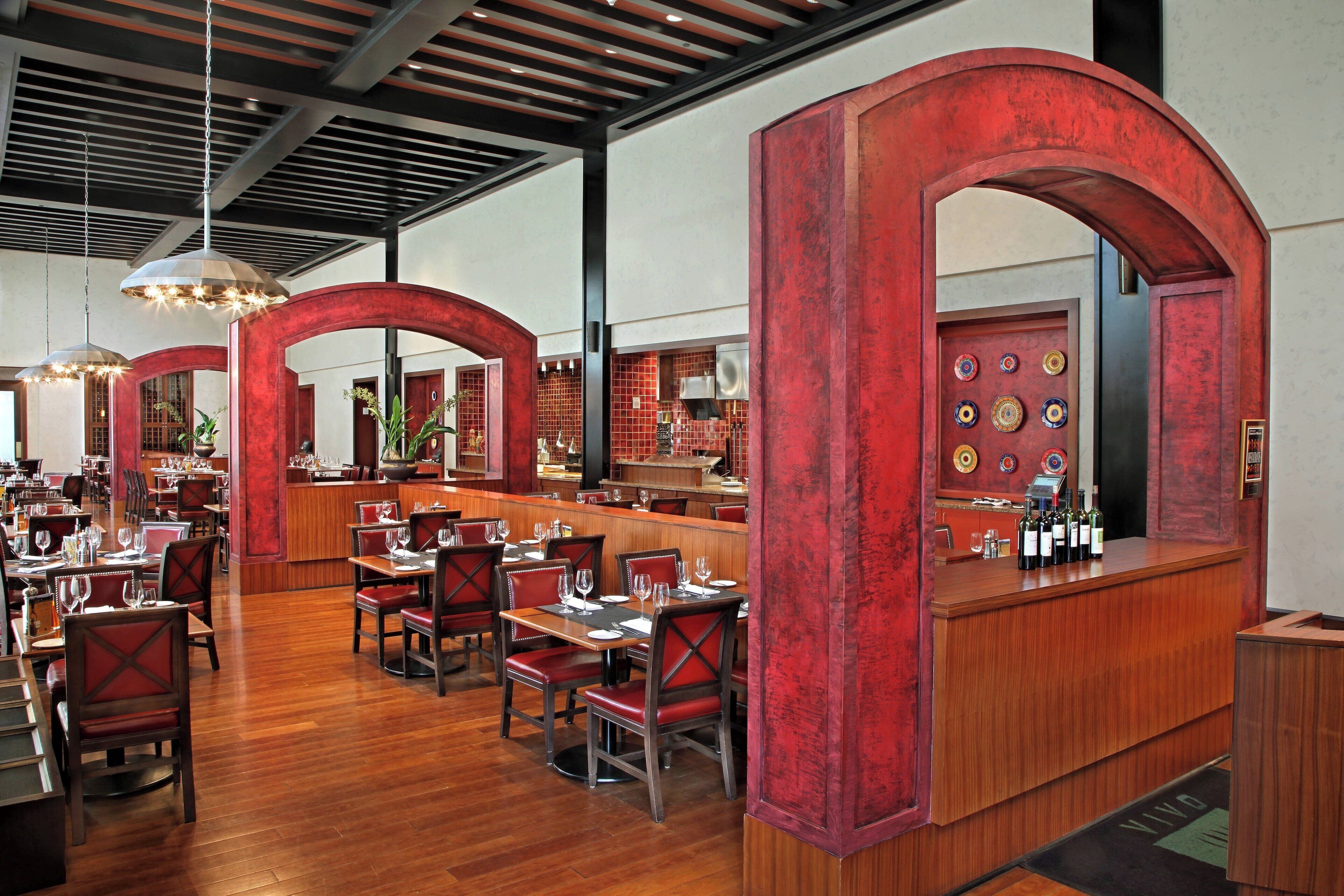 A restaurant interior with wooden tables and chairs, a bar area, and red arches.