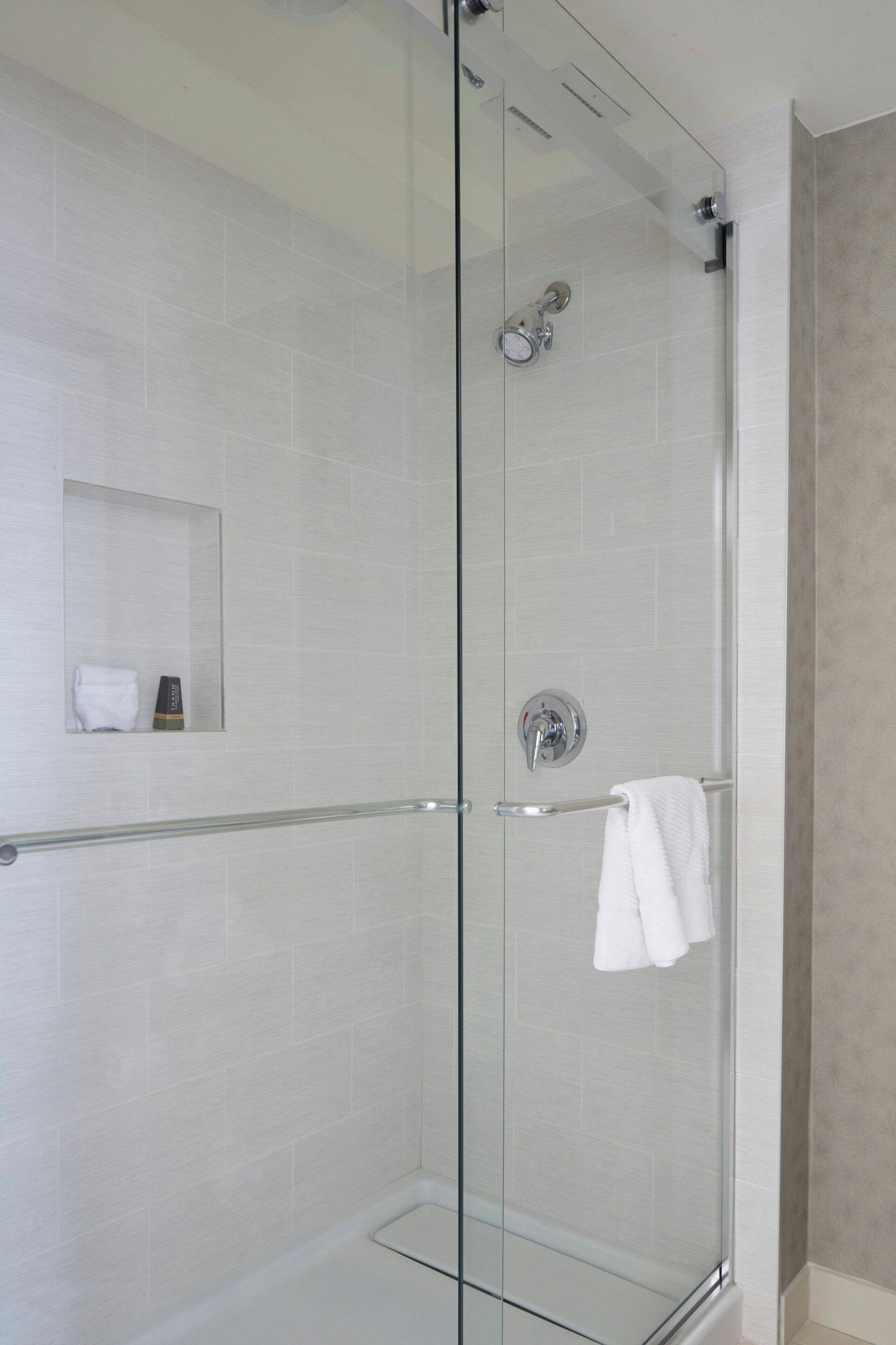 Een douche met glazen wanden en een witte handdoek aan de deurklink.