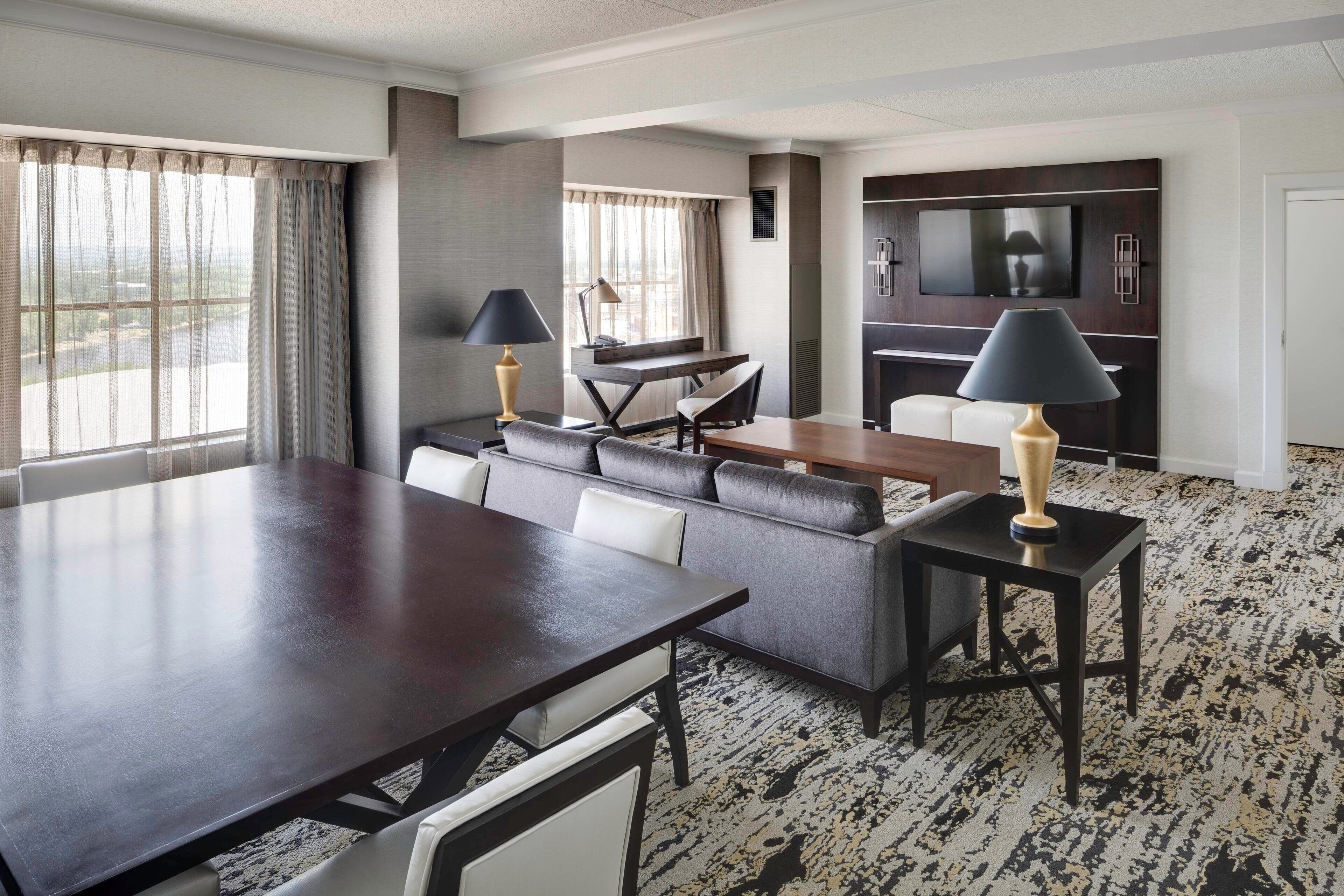 Una habitación de hotel con una gran mesa de comedor, un sofá, un televisor y un piano.