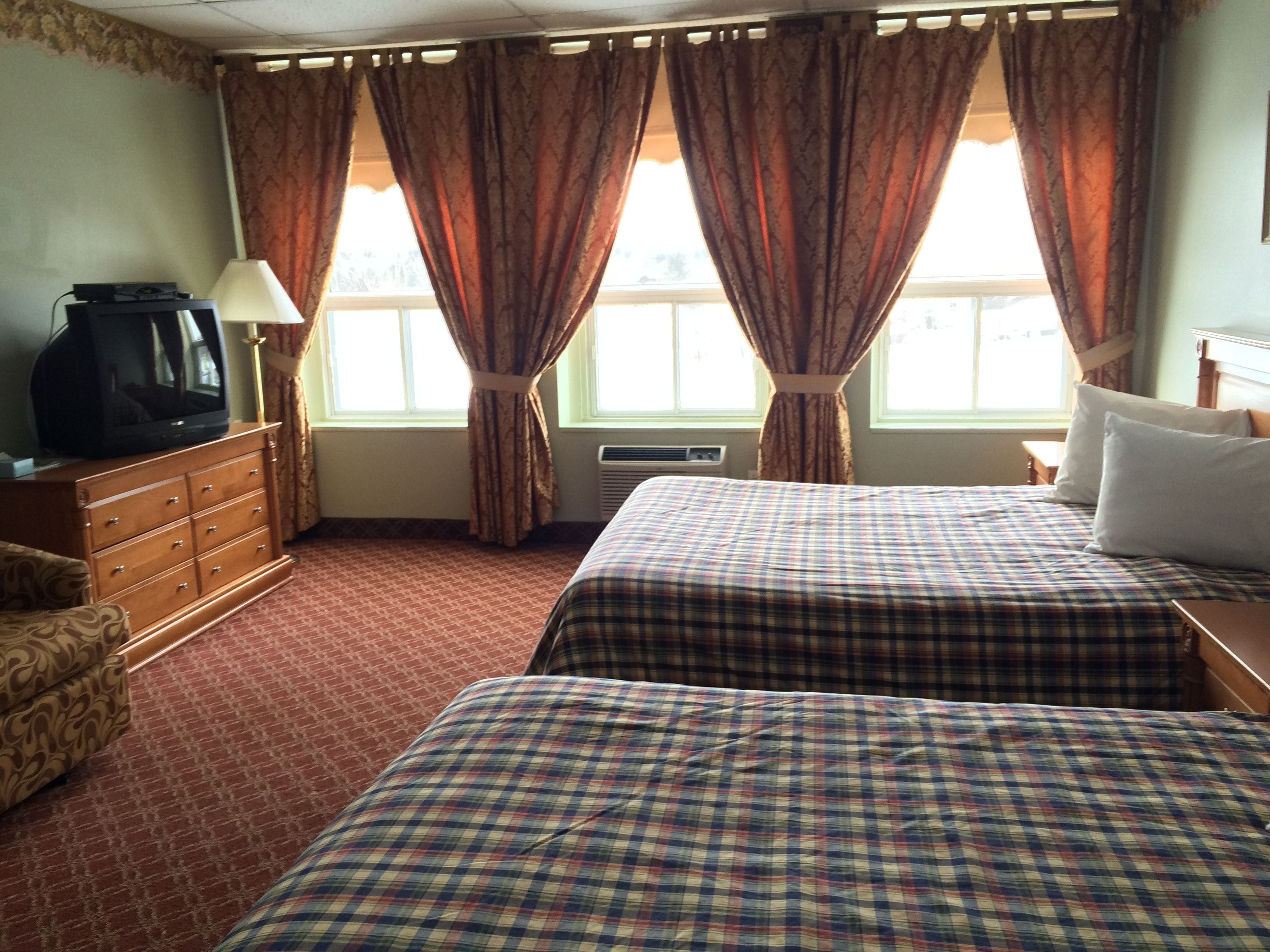 Une chambre d’hôtel avec deux lits, une commode, un téléviseur et une fenêtre avec des rideaux.
