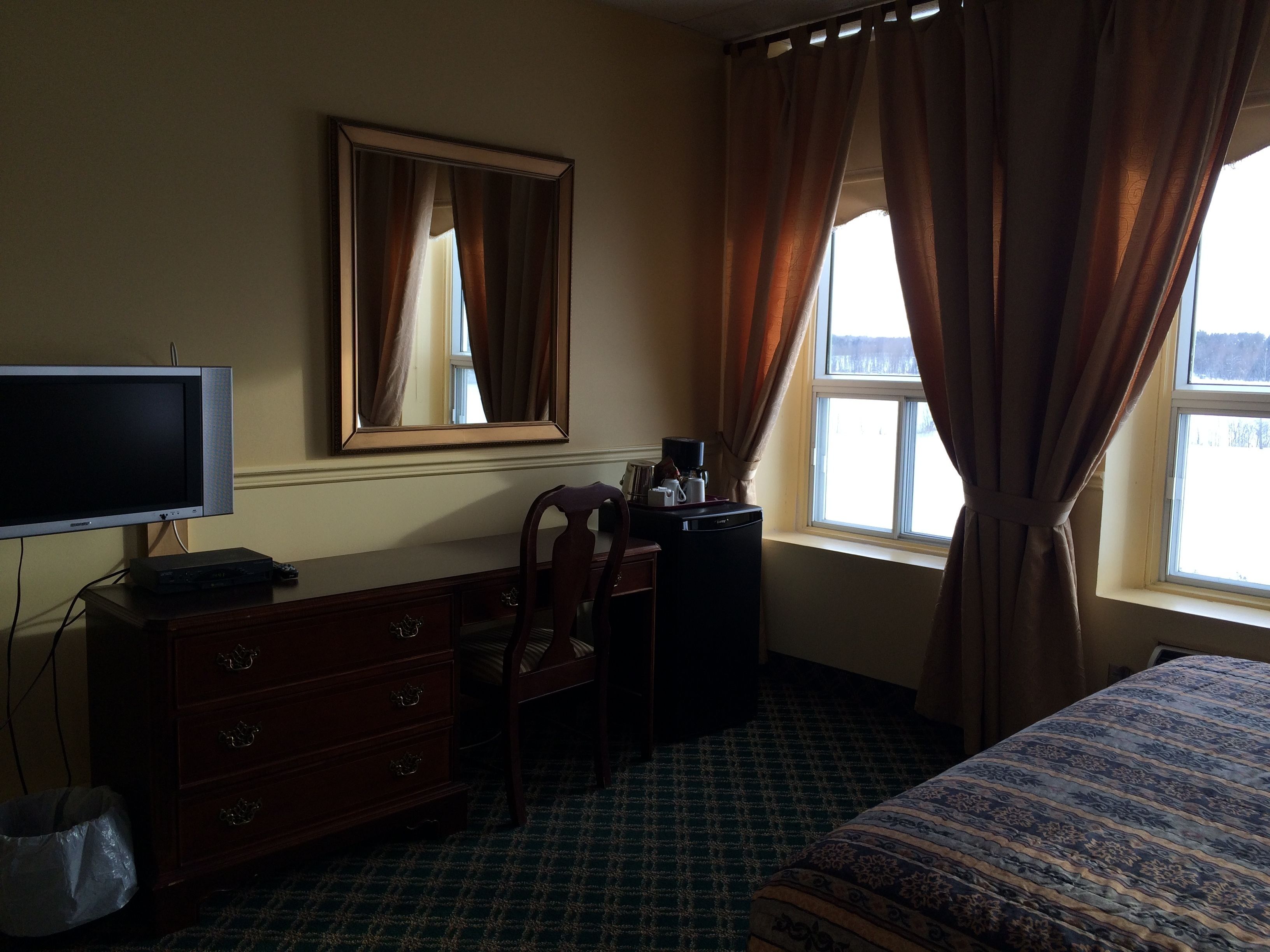 Een hotelkamer met een bed, een bureau met stoel, een dressoir, een televisie en een raam met gordijnen.