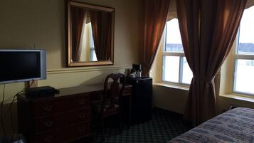 Een hotelkamer met een bed, een bureau met stoel, een dressoir, een televisie en een raam met gordijnen.