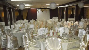 Une salle de banquet avec des tables rondes recouvertes de nappes blanches, chacune étant entourée de chaises ornées de rubans blancs.
