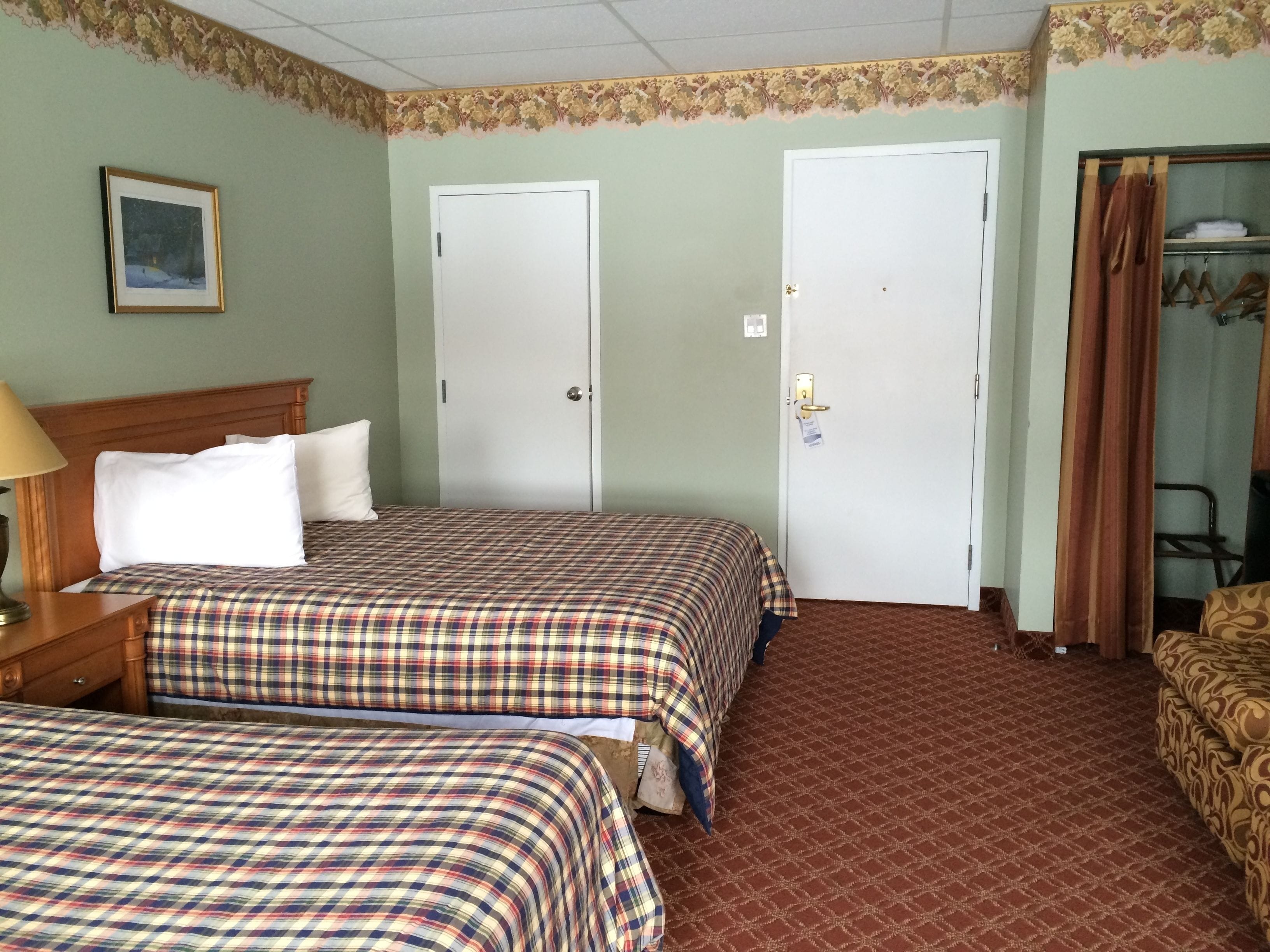 Habitación de hotel con dos camas, cabecero de madera, mesita de noche, lámpara, armario y puerta con cerradura.