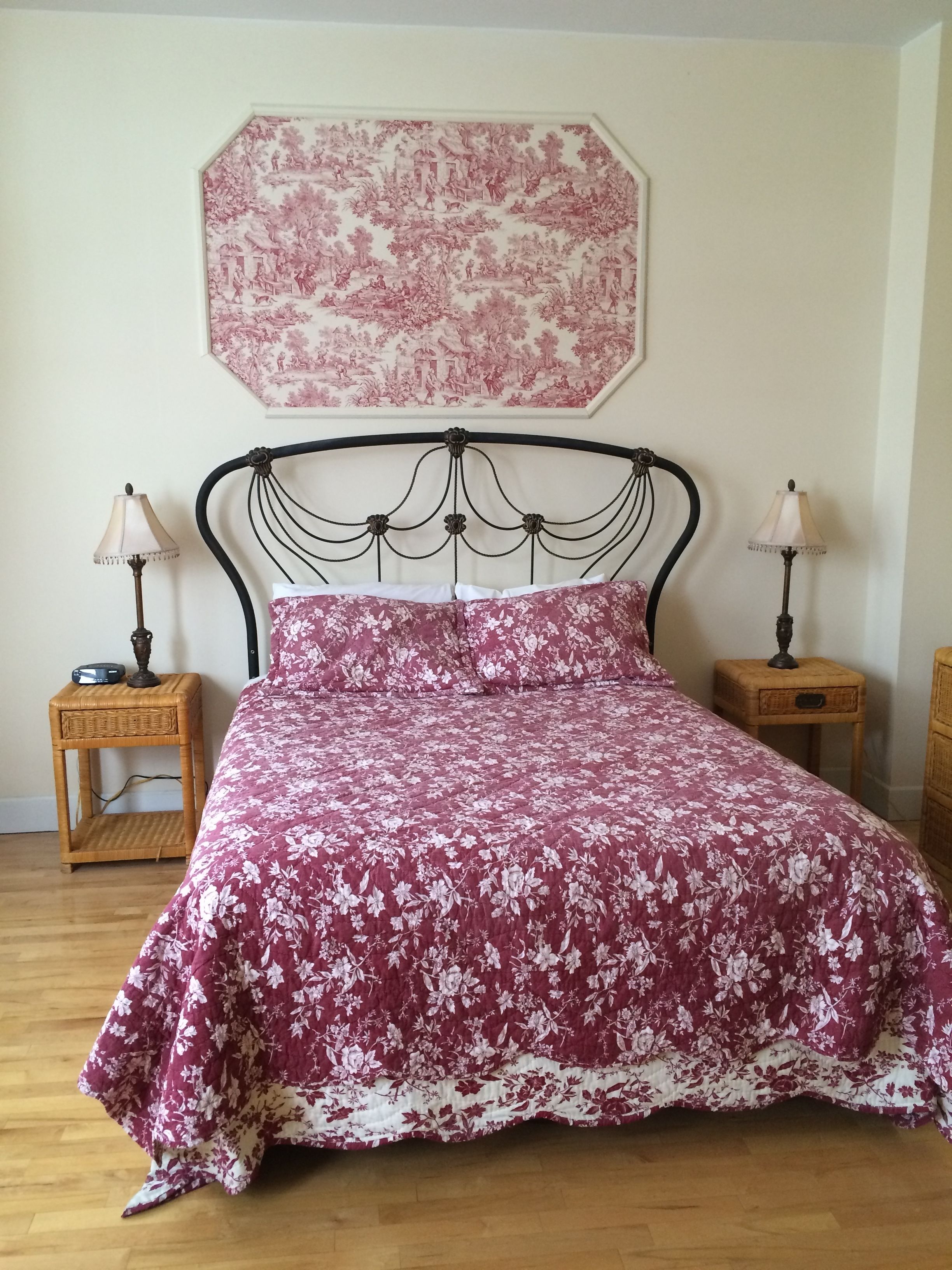 A bed with a floral bedspread, two nightstands with lamps, and a large floral artwork on the wall.