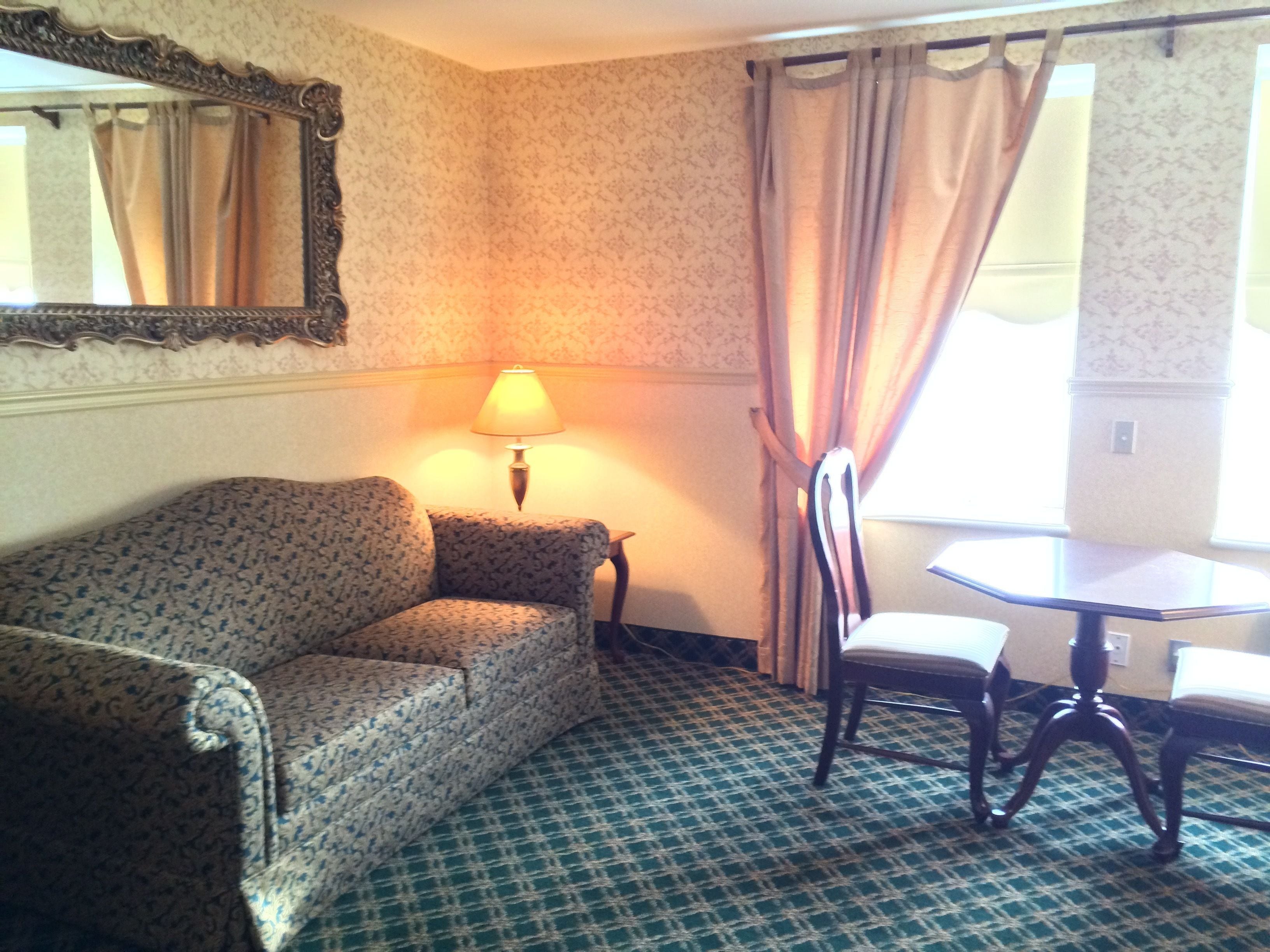 Une pièce avec un canapé à motifs, une table entourée de chaises, une lampe et une fenêtre avec des rideaux.