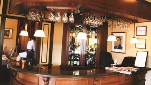 Un espace bar doté d’un comptoir en bois aux lignes courbes, de lustres en verre suspendus et de tableaux encadrés qui ornent les murs.
