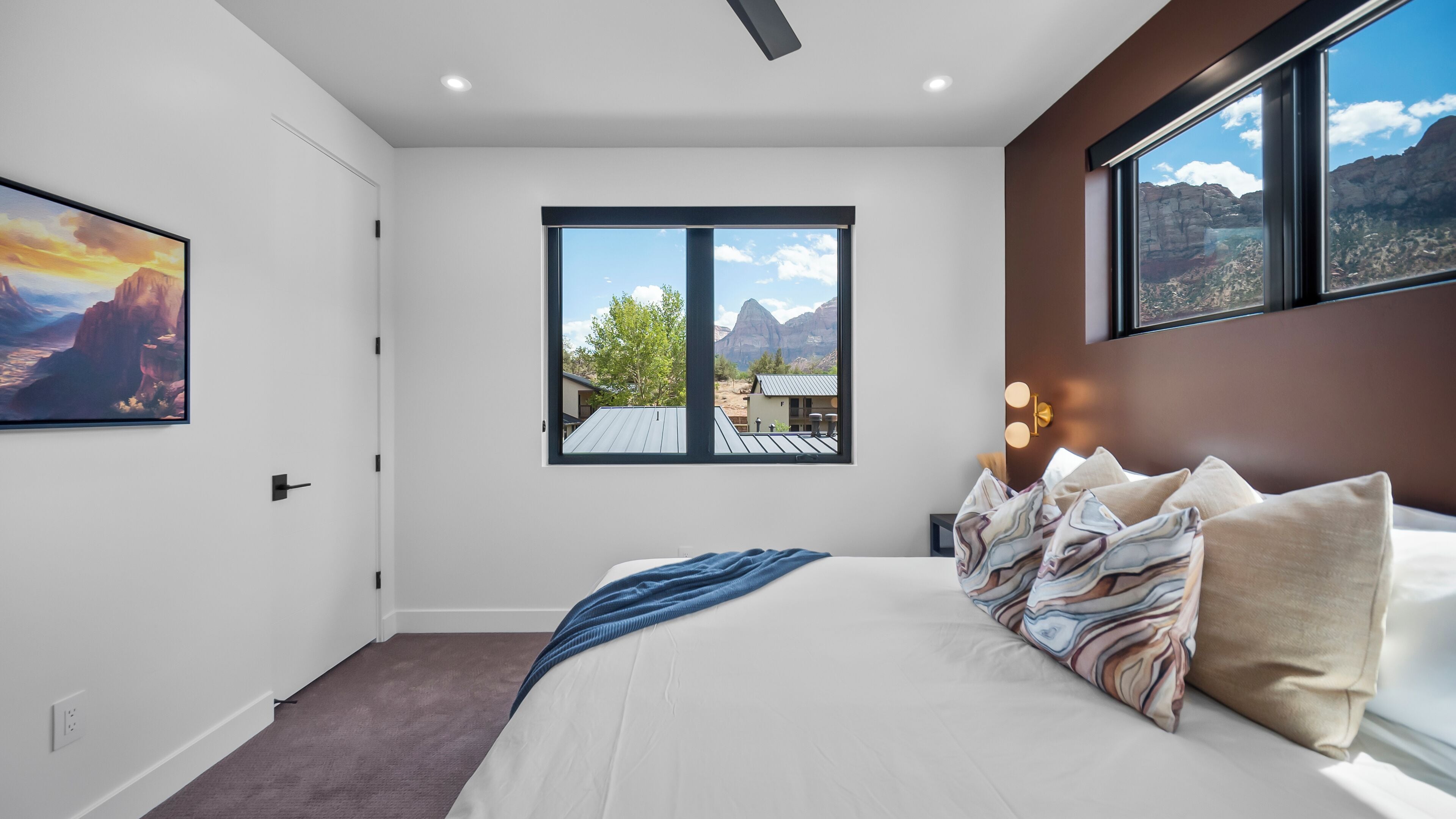 Une chambre avec un grand lit, une fenêtre donnant sur les montagnes, un ventilateur de plafond et un tableau accroché au mur.
