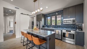 A modern kitchen with dark cabinets, stainless steel appliances, and a marble island with bar stools. - Montclair at Zion (Springdale)