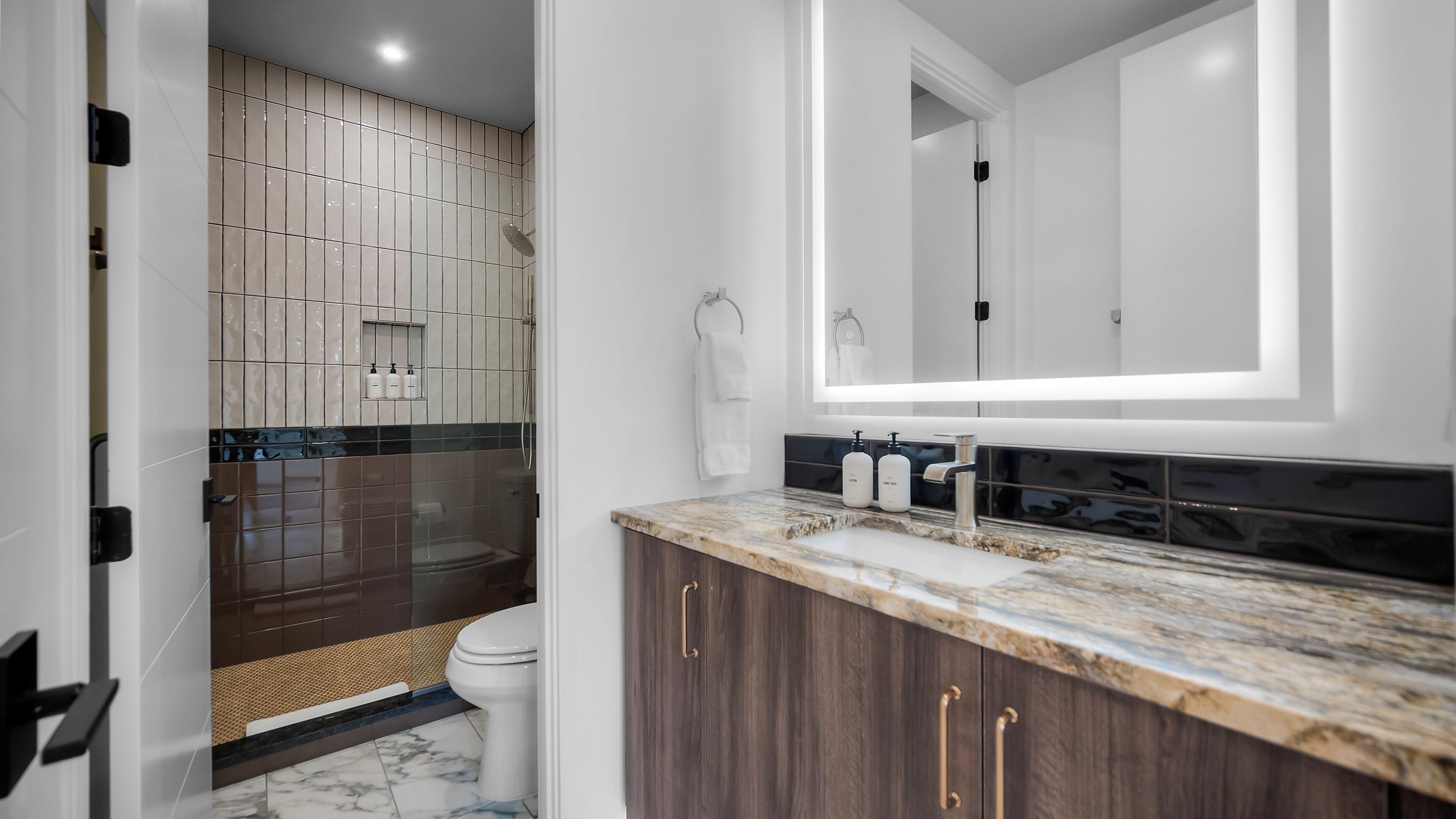A modern bathroom with a marble countertop, a large mirror, and a shower area.