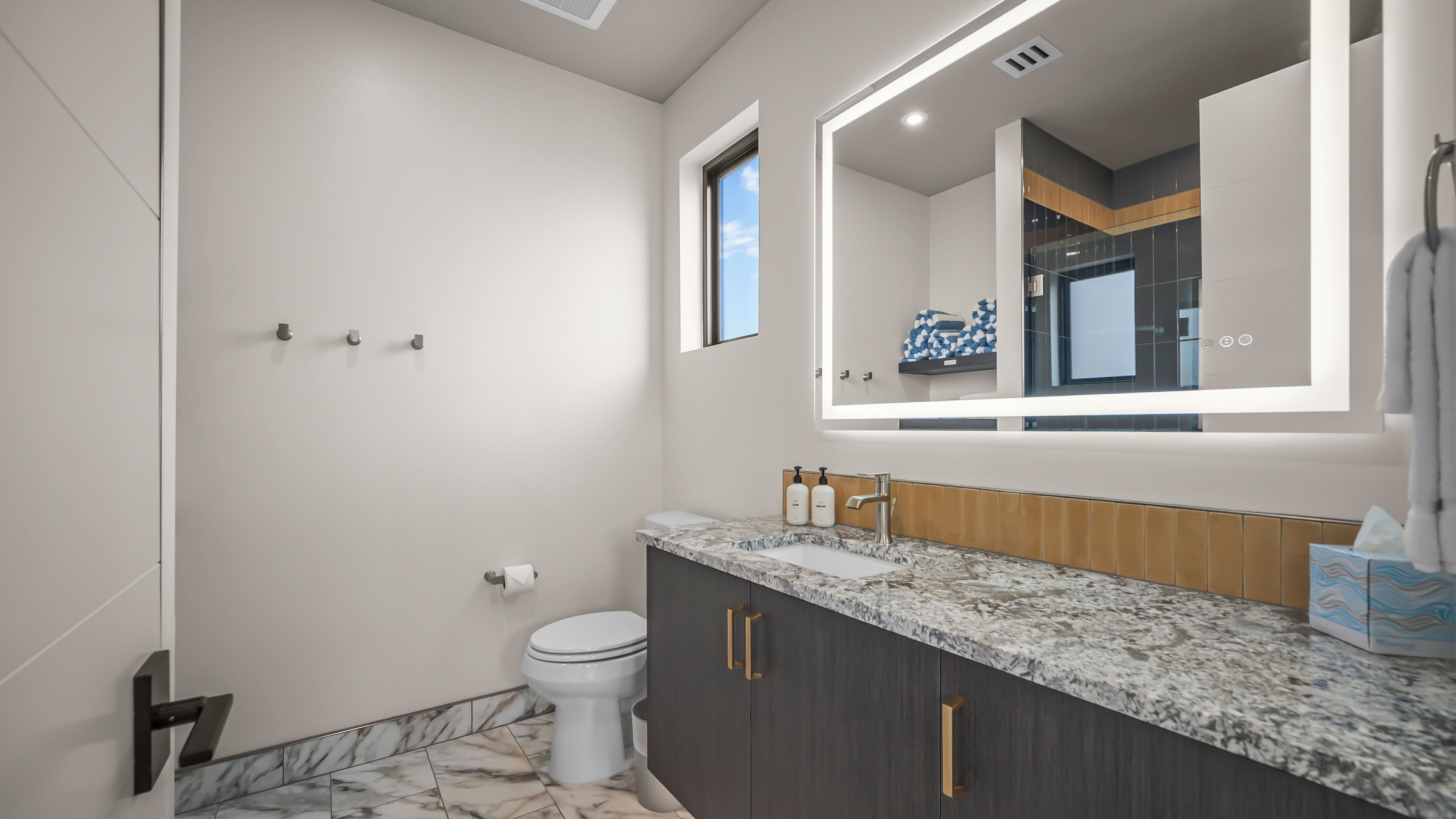 A modern bathroom with a marble countertop, a large mirror, and a toilet.