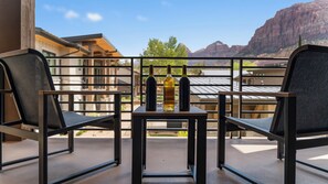 A balcony with two chairs and a table, three bottles of wine, and a view of mountains.