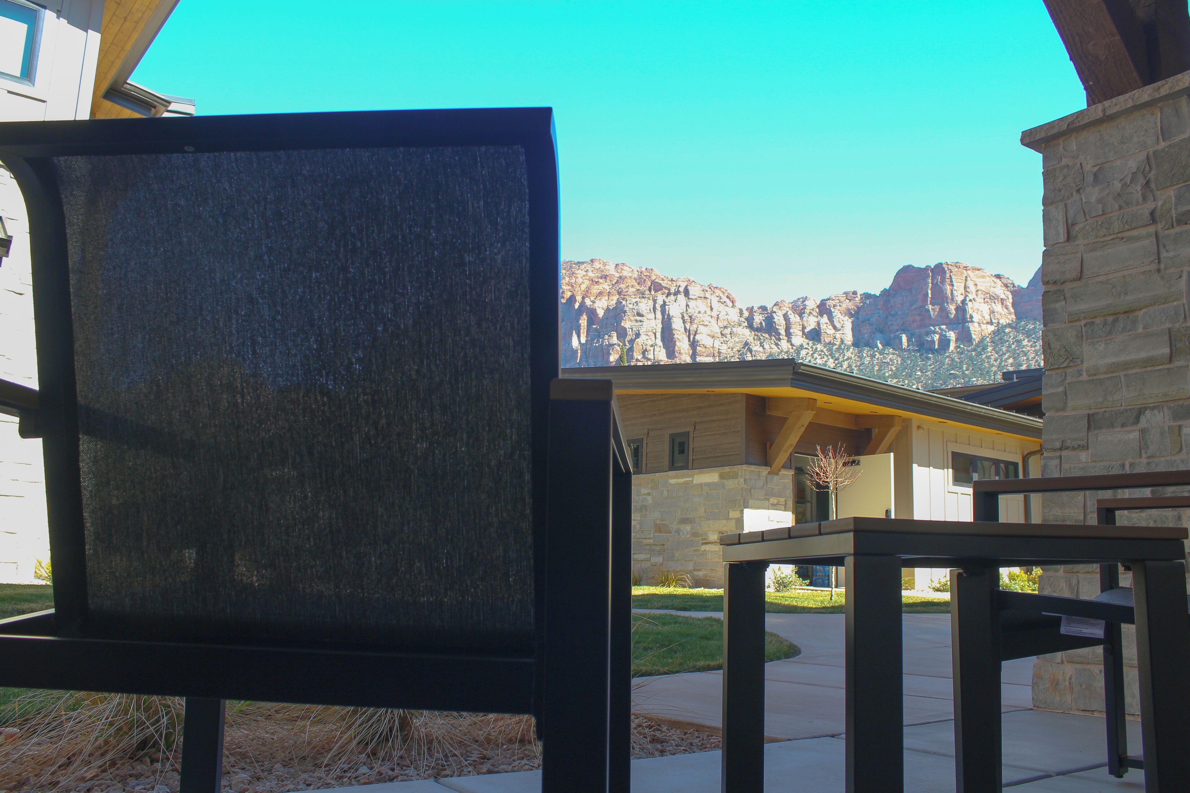 A view of a patio area with a chair and table, a stone building, and a mountain range in the background.