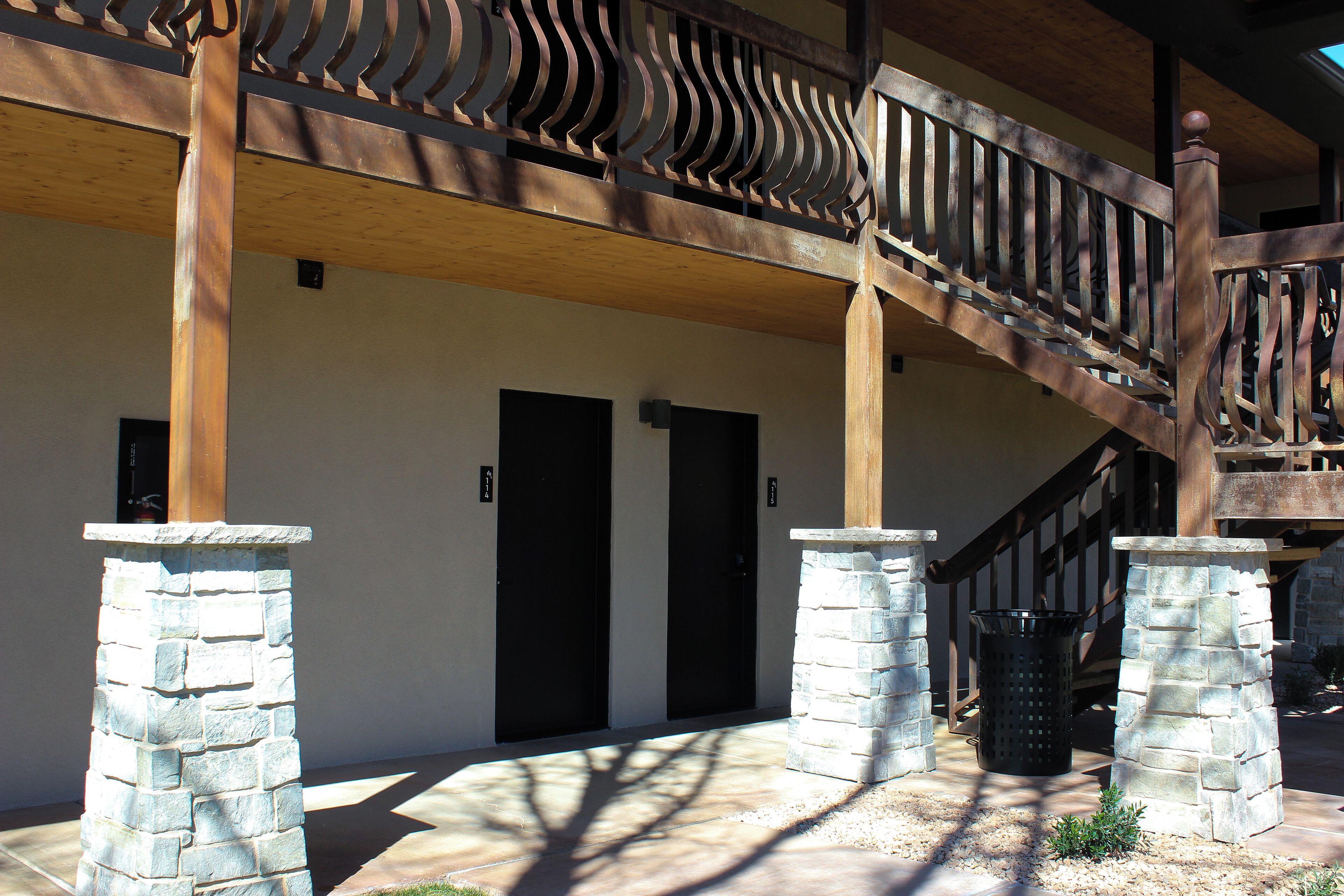 A building entrance with a wooden staircase, stone pillars, and two black doors.
