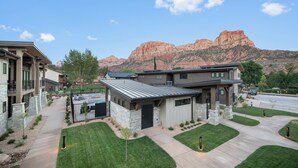 A modern two-story house with a stone facade, a swimming pool, and a view of red rock formations. - Montclair at Zion (Springdale)