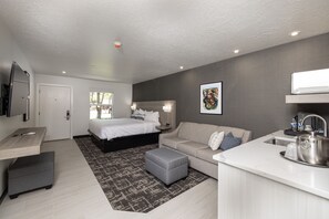 A modern bedroom with a bed, bedside tables, a desk, and a kitchenette. - Montclair at Zion (Springdale)