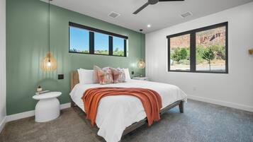 A modern bedroom with a bed, nightstands, a ceiling fan, and large windows offering a view of a rocky landscape.