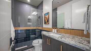 Un baño moderno con cabina de ducha de vidrio, lavamanos de mármol y un espejo grande.